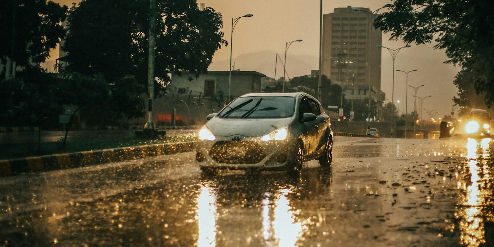 Car with headlights on driving through heavy rain on a wet city street