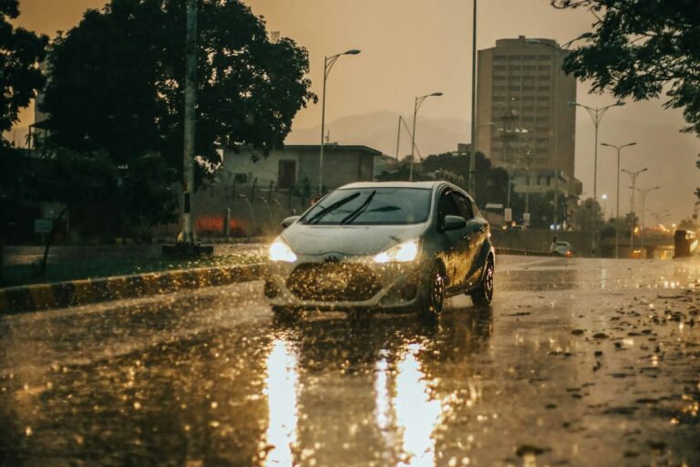 Car with headlights on driving through heavy rain on a wet city street