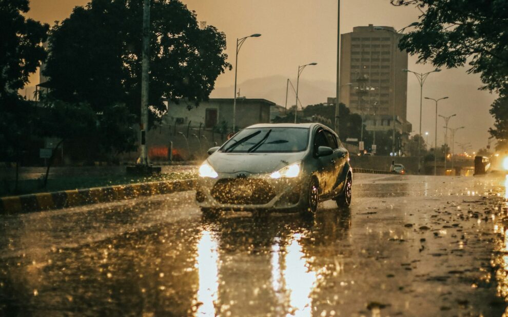 Car with headlights on driving through heavy rain on a wet city street