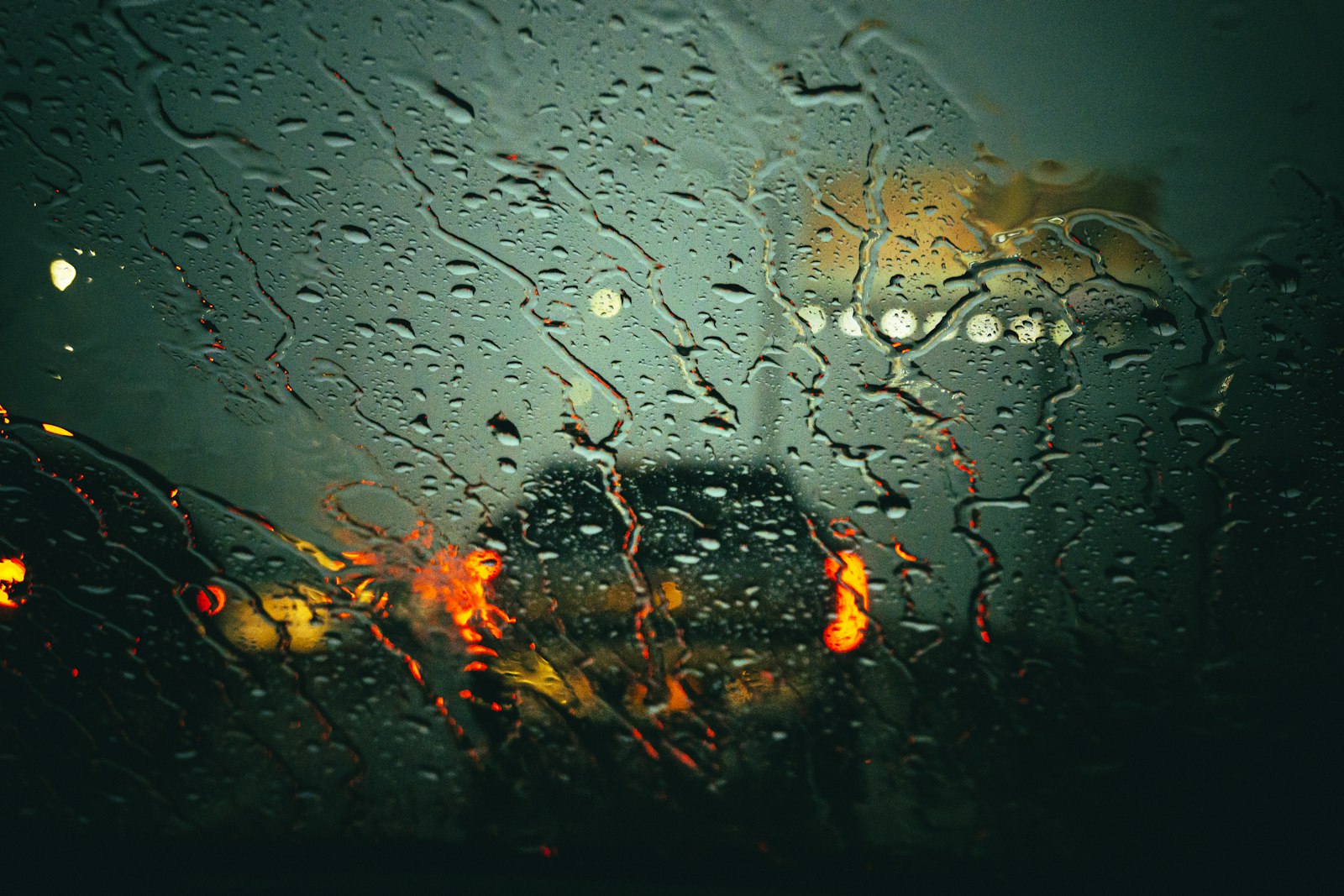 Heavy rain on a car windshield with the brake lights of the vehicle ahead blurred by water